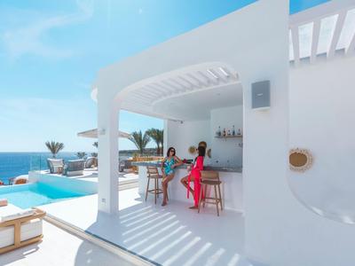 Terrazza bianca con piscina e bar, due donne godono della vista in un hotel vicino al mare.