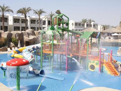 Wasserpark mit buntem Klettergerüst und Wasserspielen vor einem Hotel und Palmen.