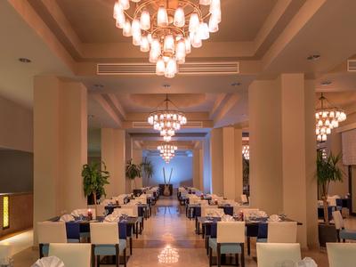 Elegant dining hall with long tables, white chairs, and chandeliers in a hotel.