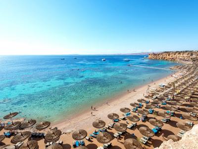 Strand mit klarem blauem Wasser, Liegestühlen und Sonnenschirmen an einer Hotelküste.