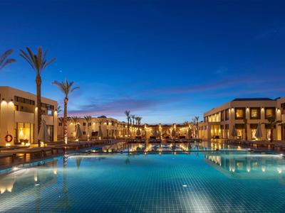 Large hotel pool at night with illuminated buildings and clear reflective water.
