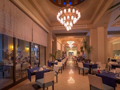 Elegant hotel restaurant with chandeliers, blue chairs, and large windows at dusk.