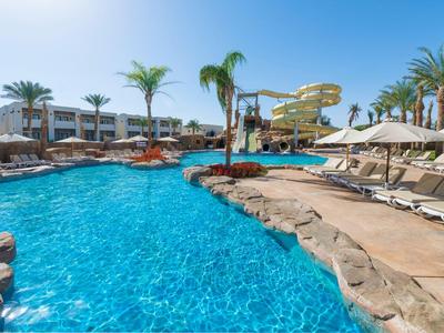 Großer Hotelpool mit blauen Wasser, Wasserrutsche und Liegestühlen unter Palmen.