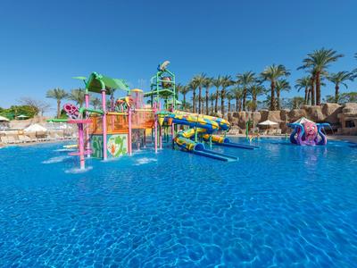 Colorful water playground with slides in a large pool under blue sky and palm trees.
