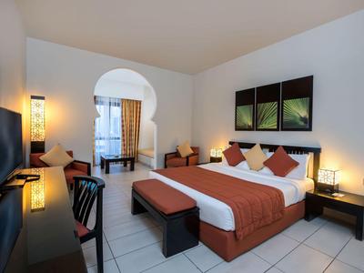 Modernes Hotelzimmer mit großem Bett, Sitzbank, Schreibtisch und Zugang zu einem Balkon.
