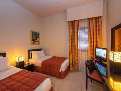 Hell eingerichtetes Hotelzimmer mit zwei Einzelbetten, Schreibtisch und dekorativer Beleuchtung.