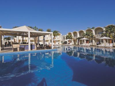 Large pool in front of a hotel with sun umbrellas under a clear blue sky.