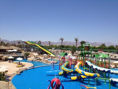 Wasserpark mit bunten Rutschen und Liegestühlen, umgeben von Palmen und Bergen.