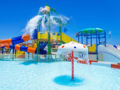 Bunter Wasserspielplatz mit Wasserrutschen und einem Pilz-Wasserbrunnen unter klarem Himmel.