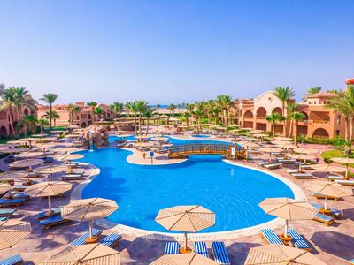 Großer Hotelpool mit Sonnenschirmen und Palmen unter blauem Himmel.