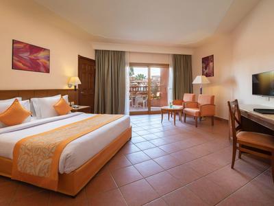 Habitación de hotel luminosa con cama doble, escritorio, televisión y balcón con vistas.
