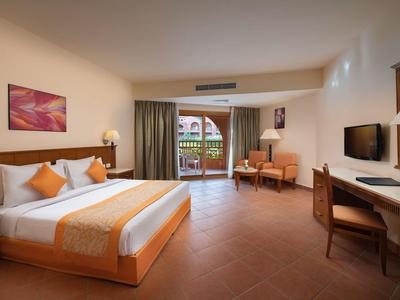 Habitación de hotel luminosa con balcón, cama doble y escritorio.