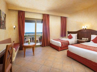 Habitación de hotel luminosa con dos camas, balcón y vista al mar.