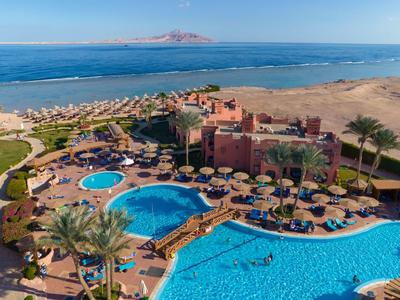 Hotel con varias piscinas, sombrillas y acceso directo a la playa de arena junto al mar.