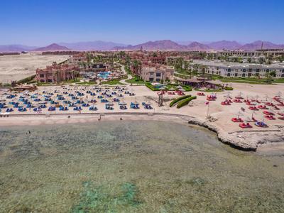 Breiter Sandstrand mit Liegen und Sonnenschirmen vor Hotelanlagen in Wüstenumgebung.
