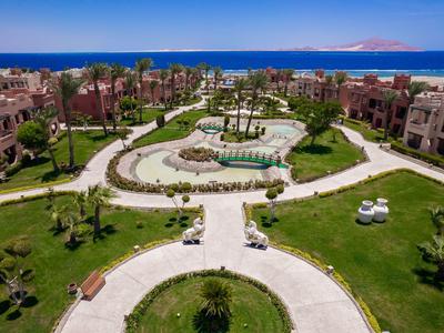 Hotelanlage mit gepflegten Wegen, üppigen Gärten und Blick auf das Meer im Hintergrund.