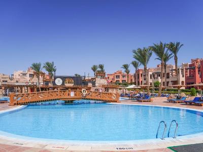 Großer runder Hotelpool mit blauer Wasserfläche, umgeben von Liegestühlen und Palmen.