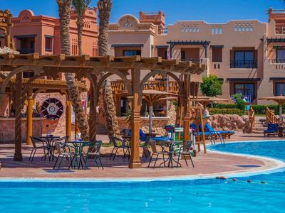 Hotelpool mit blauer Wasseroberfläche, umgeben von Sonnenschirmen, Stühlen und Gebäuden im Hintergrund.