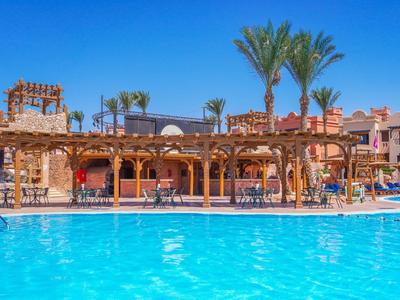 Freizeitpool mit klarem blauem Wasser und Sonnenschirmen neben Hotelgebäuden bei sonnigem Himmel.