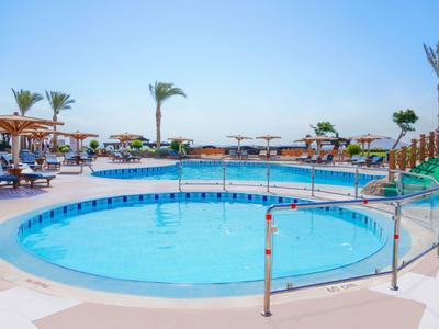 Rundlicher Pool mit klar blauem Wasser, umgeben von Liegestühlen und Palmen unter klarem Himmel.