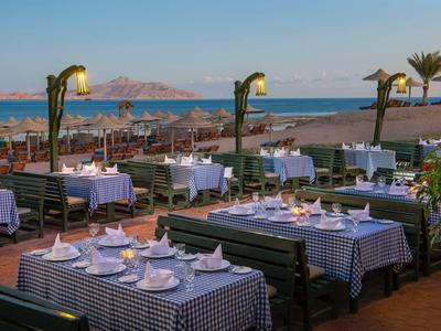 Terraza de restaurante con manteles a cuadros azules y vista al mar al atardecer.