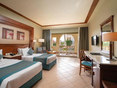 Habitación de hotel luminosa con dos camas individuales, balcón con vista al mar, mobiliario elegante y suelo de baldosas.