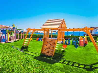 Kinderspielplatz mit Holzgerüsten und Rutschen auf grünem Rasen unter klarem, blauem Himmel.