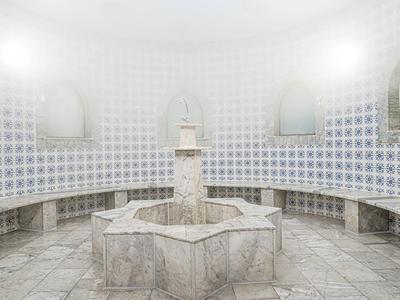 Ein helles, runder Raum mit einem zentralen Springbrunnen und halbrunden Sitzbänken entlang der Wände.
