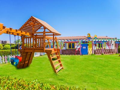 Kinderspielplatz mit Klettergerüst und Rutsche auf grünem Rasen vor Gebäude in klarem Himmel.