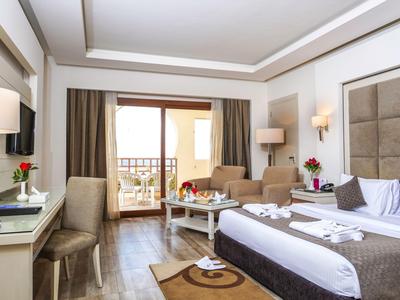 Modernes Hotelzimmer mit Doppelbett und Sitzbereich, Balkon mit Blick auf einen Urlaubsort.