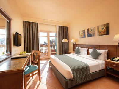 Helles Hotelzimmer mit großem Bett, Schreibtisch, Stuhl und Balkon mit Blick nach draußen.