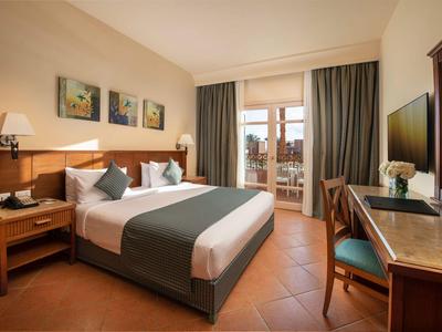 Helles Hotelzimmer mit Doppelbett, Nachttischen, Schreibtisch und Zugang zum Balkon mit Stadtblick.