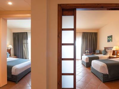 Hotelzimmer mit zwei Einzelbetten, Holzmöbeln und Fenstern mit Vorhängen.