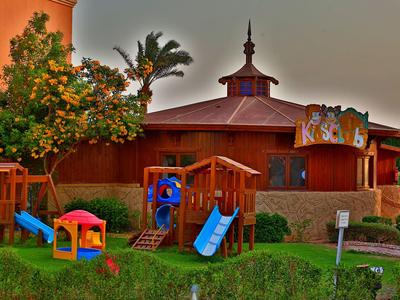 Bunter Kinderspielplatz mit Rutschen vor einem runden Holzhotelgebäude und Palmen bei Sonnenuntergang.