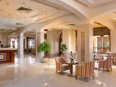 Heller Hotellobby mit Rezeption, Sitzbereich und großen Bögen in gedeckten Farben.