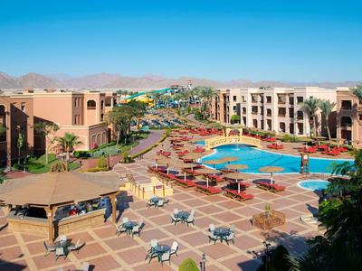 Großer Hotelkomplex mit Pool, Liegestühlen und trockenem Bergpanorama bei klarem Himmel.