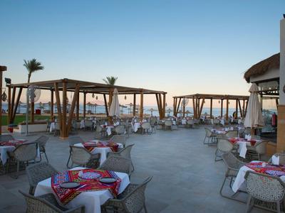 Restaurant en plein air avec tables dressées et auvents en bois au coucher du soleil près de la mer.
