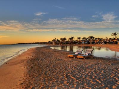 Ein ruhiger Strand mit Sonnenliegen und Palmen bei Sonnenuntergang an einem Urlaubsort.