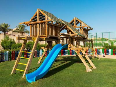 Kinderspielplatz mit Holzhaus, blauer Rutsche und Klettergerüst auf einem grünen Rasen.