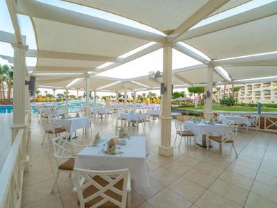 Offener Restaurantbereich mit weißen Tischen und Stühlen neben einem Hotelpool.