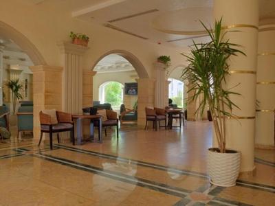 Heller Hotellobby mit Säulen, Sitzbereichen und einer großen Topfpflanze nahe dem Eingang.