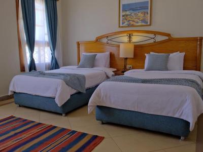 Hotelzimmer mit zwei Einzelbetten, weißen Bettdecken und einem bunten Streifen-Teppich.
