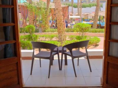 Blick von einem Hotelzimmer auf eine Terrasse mit zwei Stühlen und einem Tisch vor Palmen.