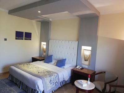 Chambre d'hôtel avec grand lit blanc, deux oreillers bleus, tables de chevet et deux lampes murales.