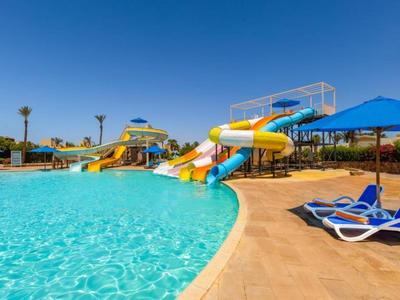 Un parc de toboggans aquatiques ensoleillé avec une piscine claire et des chaises longues bleues le long du bord.