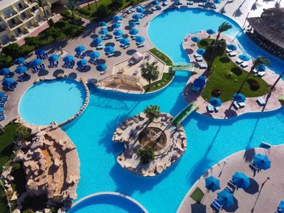 Grande piscine d'hôtel avec palmiers, îles et de nombreux parasols bleus sur la terrasse.