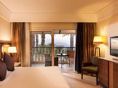 Gemütliches Hotelzimmer mit großem Bett, Balkon und Blick auf Bäume und Berge.