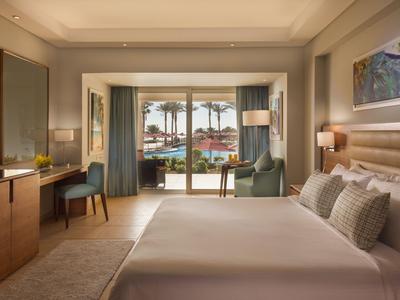 Modernes Hotelzimmer mit großem Bett, Sesseln und Meerblick durch breite Glasfenster.