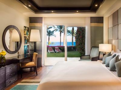 Helles Hotelzimmer mit großem Bett, Schreibtisch und Blick auf tropischen Garten und Meer.