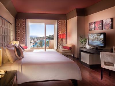 Modern eingerichtetes Hotelzimmer mit großem Bett, TV und Balkon mit Aussicht auf Stadt und Wasser.
